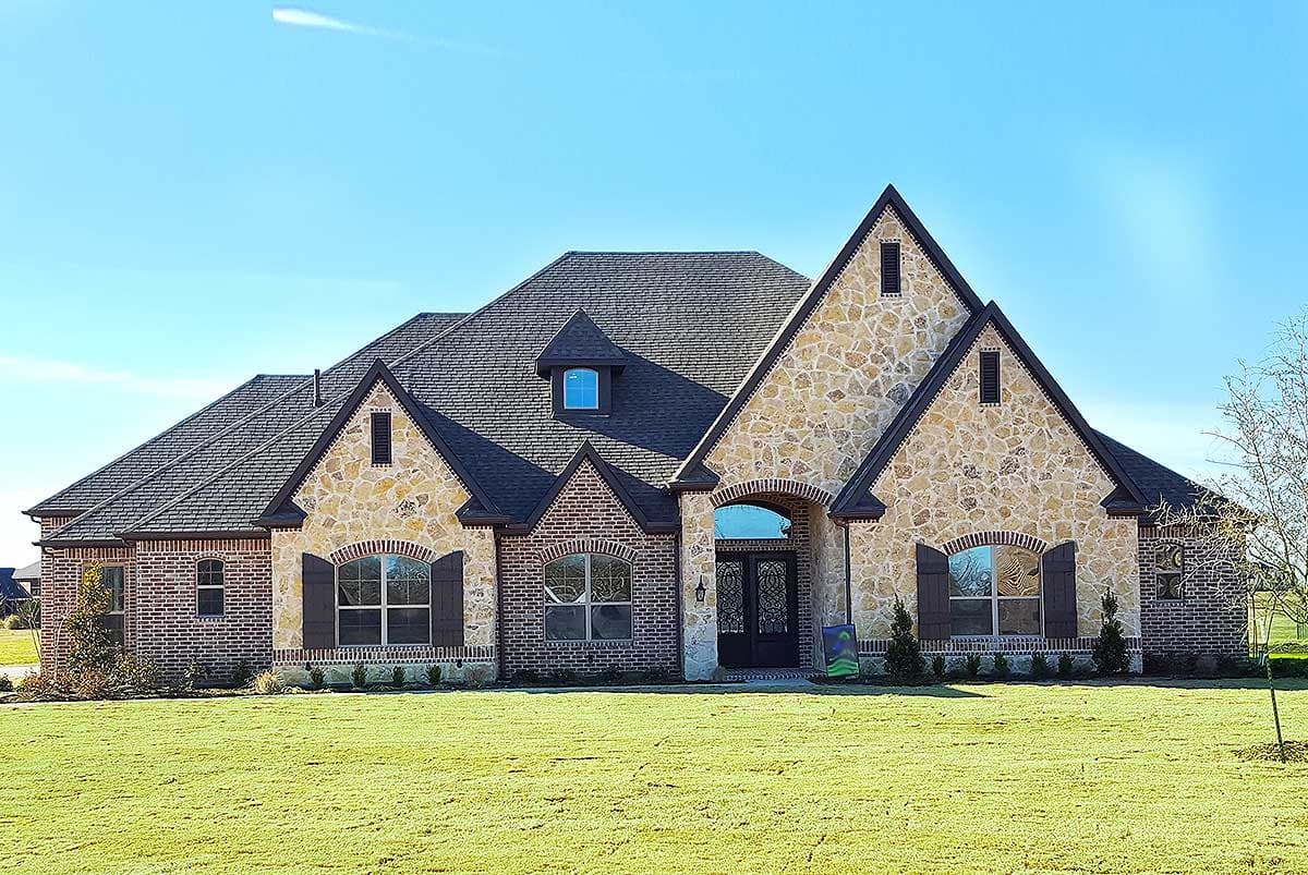 House plan exterior of a one-story home with stone and brick facade, prominent gables, arched entryway, and dark shutters.