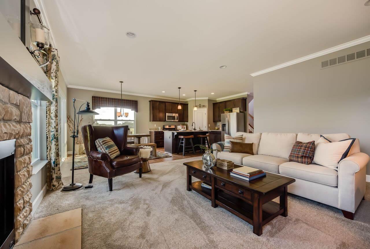 Interior view of living area and kitchen with stone fireplace, large sectional, island, and dark wood cabinetry.