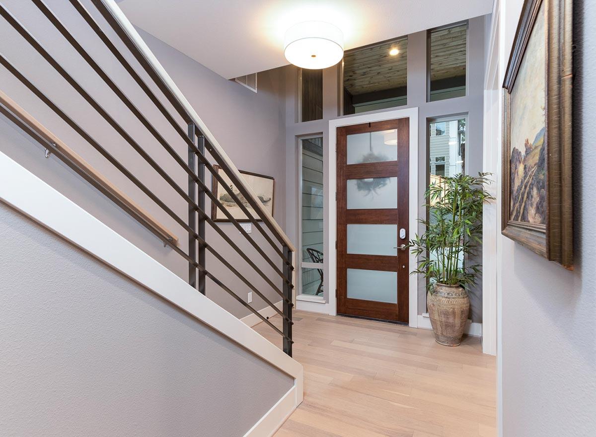 Modern entryway with wood door, frosted glass panels, metal railing, and wood floor.
