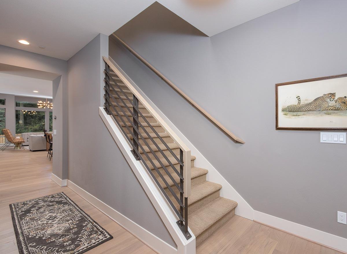 Interior view of a staircase with carpeted treads, metal railing, wood handrail, and light wood flooring.