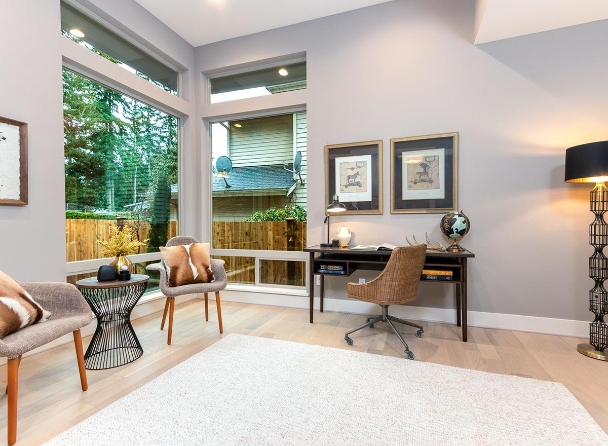 Home office with large corner windows, a desk with chair, and two framed art pieces.