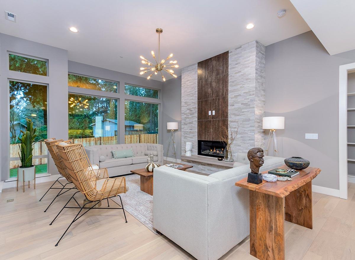 Living room interior with sectional sofa, fireplace, and large windows. Features vaulted ceiling, stacked stone accent wall, and modern lighting.