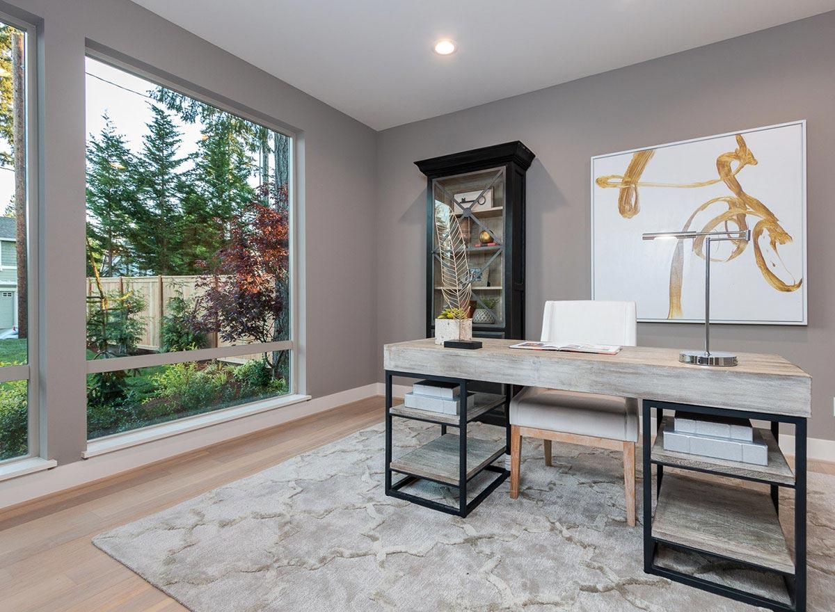 Home office interior with large windows, a modern desk, shelving unit, and abstract art.