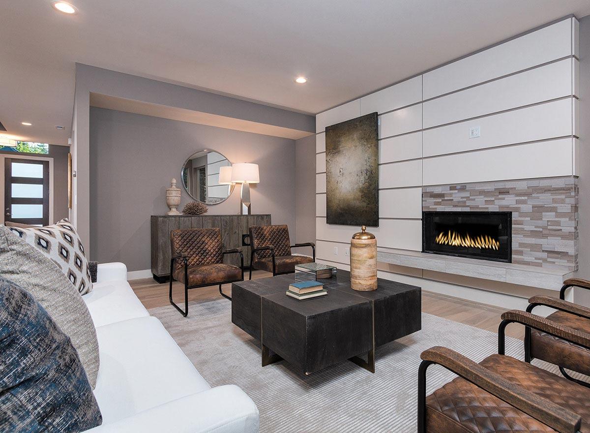 Living room with white sofa, textured chairs, geometric coffee table, and fireplace with stacked stone surround.