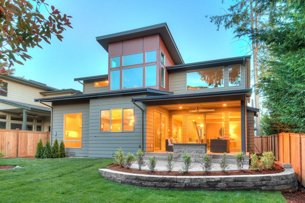 Modern house plan exterior with large windows, layered rooflines, and covered patio with outdoor seating.