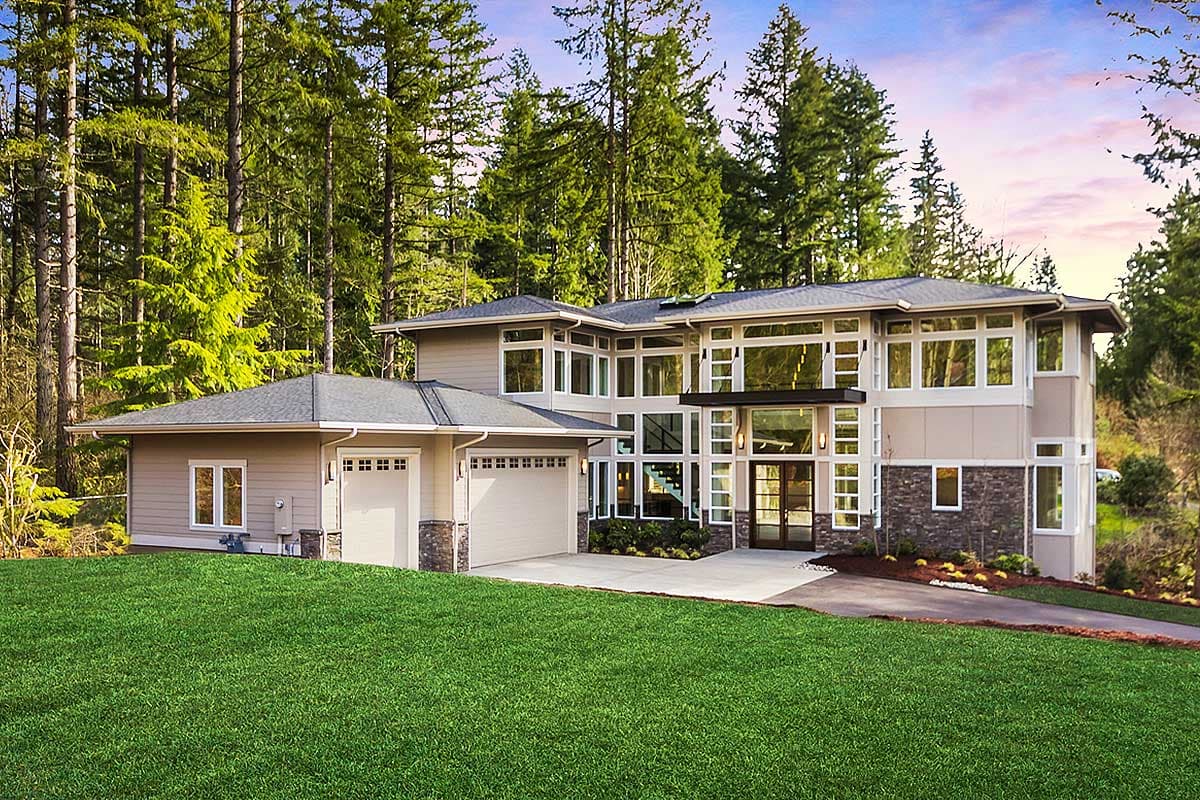 House plan exterior. Two-story modern home with large windows, flat roof, and attached garage. Stone accenting and a landscaped yard are visible.