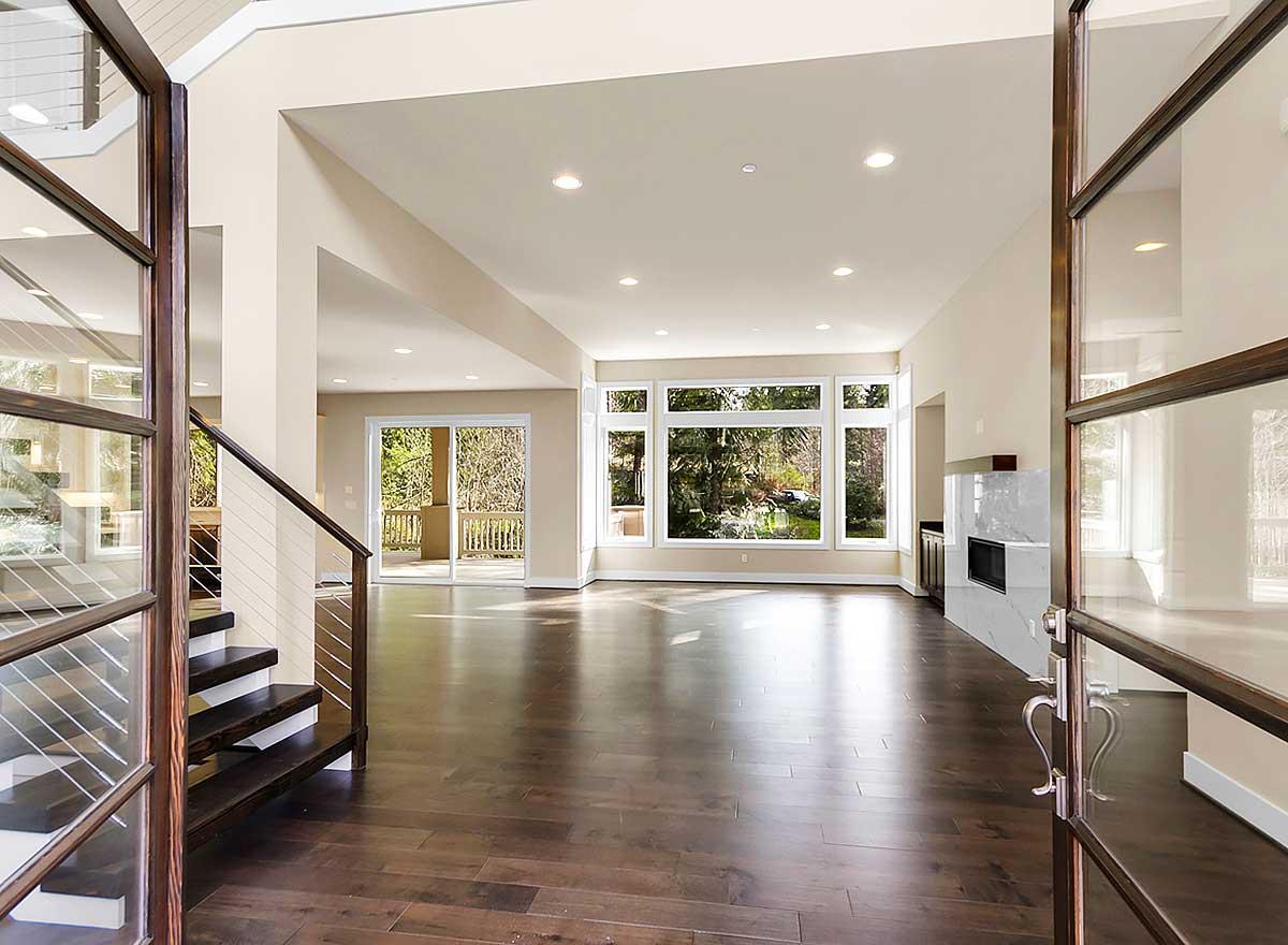 Open concept living space with modern fireplace, large windows overlooking backyard, and dark wood staircase.