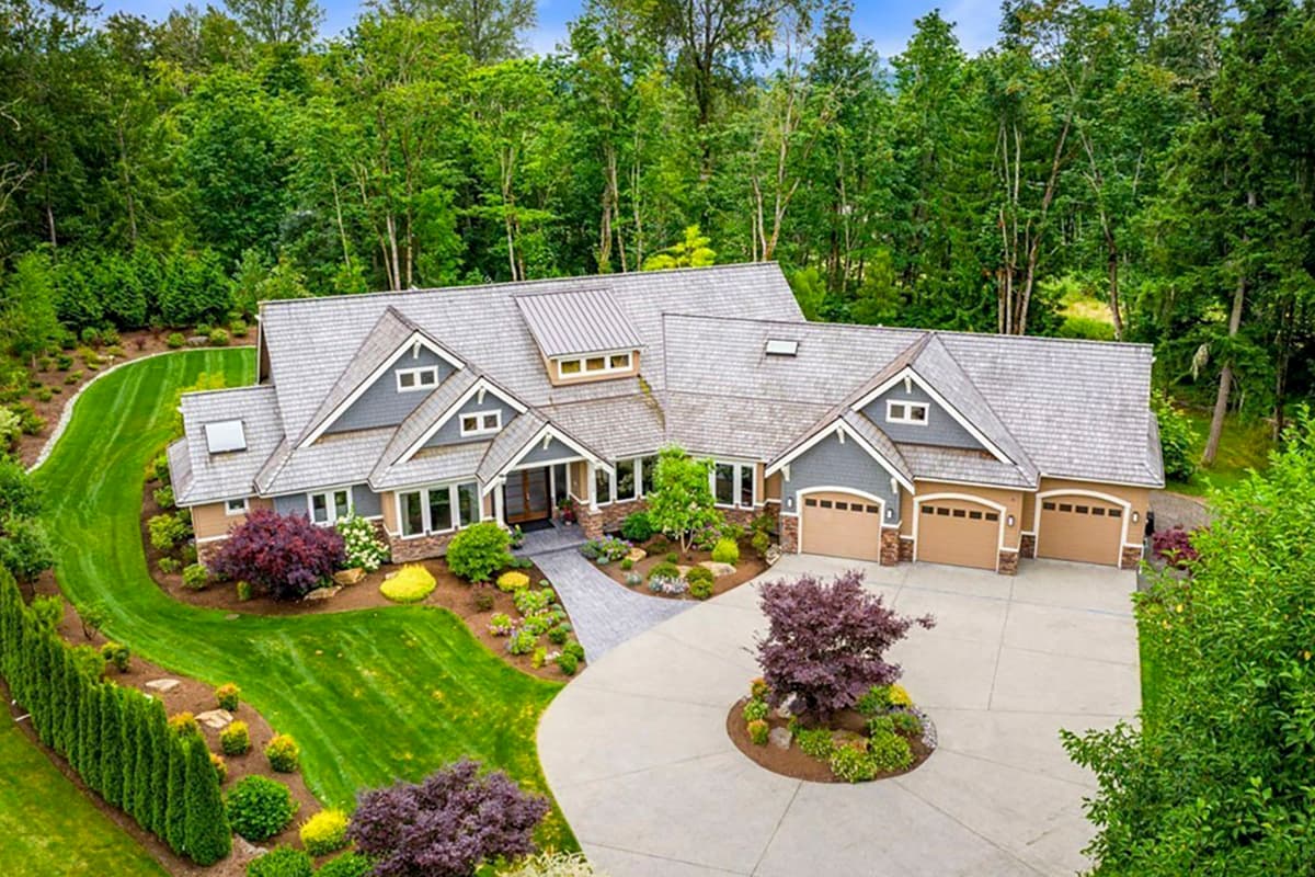 House plan exterior. Two-story with gabled roof, dormers, and attached three-car garage. Landscaped front yard with driveway.