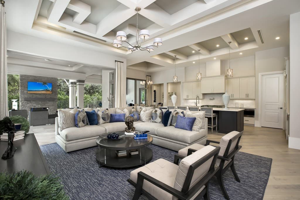 Open concept living area with coffered ceiling, sectional sofa, fireplace, and adjacent kitchen with island.