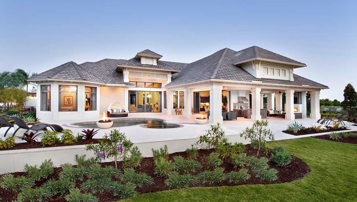 Exterior view of a luxurious home with a pool, patio, and outdoor kitchen. Landscaping includes green lawn and flower beds.