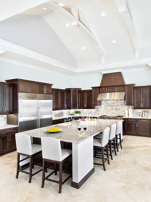A modern kitchen with a large island, granite countertops, stainless steel appliances, and dark wood cabinetry.