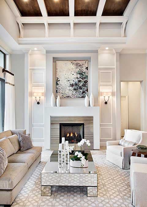 Elegant living room with fireplace, abstract art, and beige sofa. Mirrored coffee table with decor and patterned rug.
