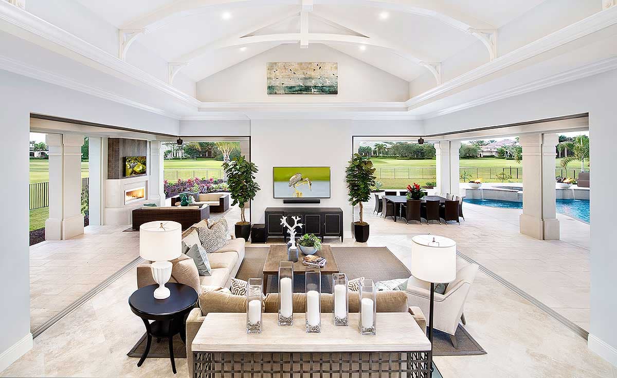 Luxury open-concept living room with outdoor access, including fireplace, TV, dining area, and pool. Features vaulted ceilings and modern decor.