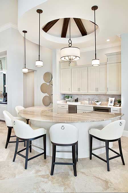 Luxurious kitchen with a marble-topped curved island, white bar stools, and pendant lights.