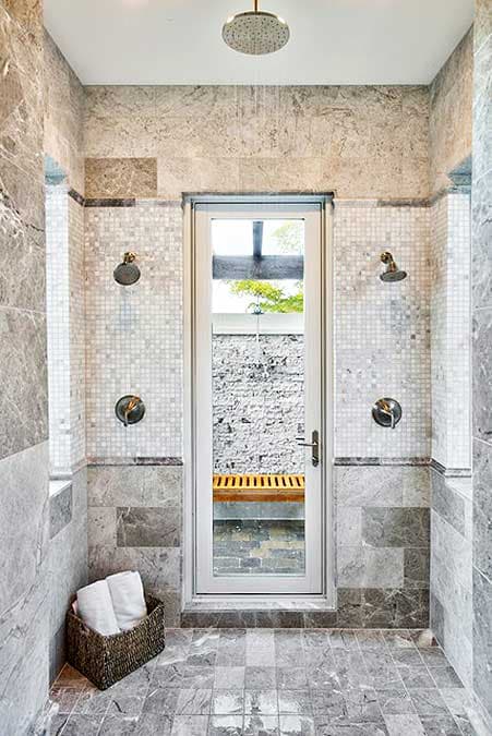 Luxurious tiled shower with rain shower head and dual shower heads, a door leads to an outdoor shower area.