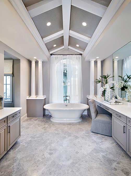 Luxurious bathroom with white clawfoot tub, grey marble floor, and vaulted ceiling with white beams.