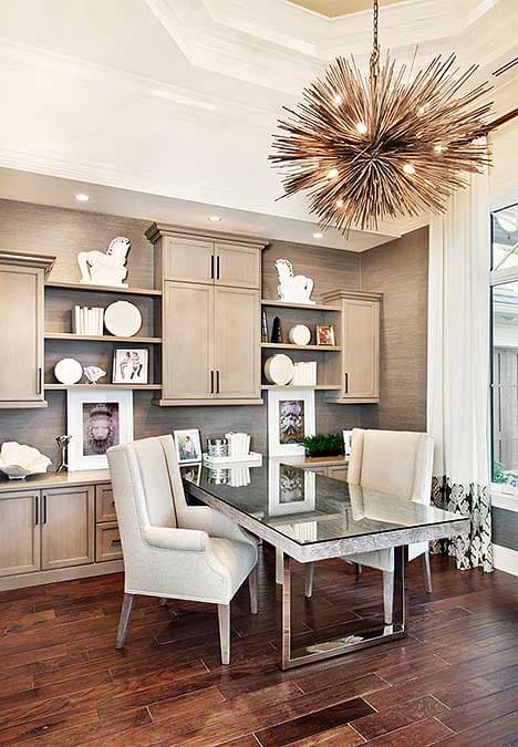 Luxurious home office with a large glass table, modern chairs, and a unique sputnik chandelier. Built-in cabinets and shelves.
