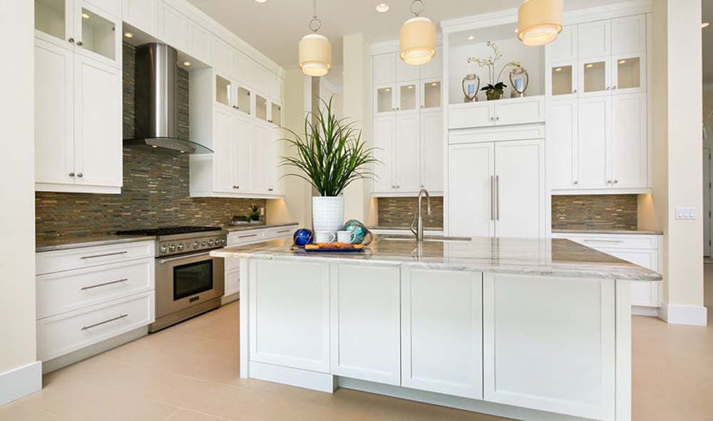 Interior view of a kitchen with a large island, white cabinetry, stainless steel appliances, and a stone tile backsplash.