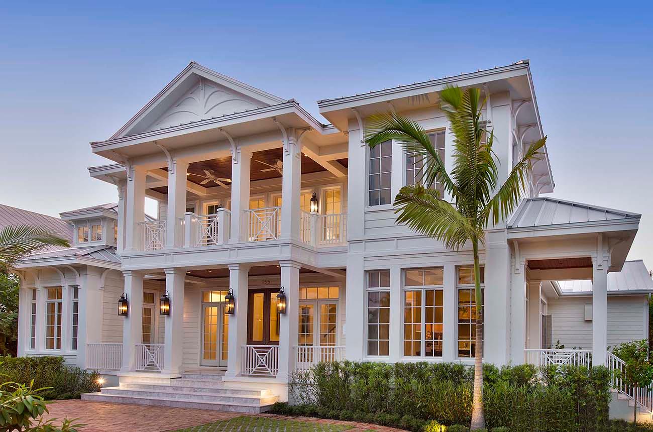 Two-story house plan exterior with wide covered balconies, white railings, multiple gables, and metal roof.