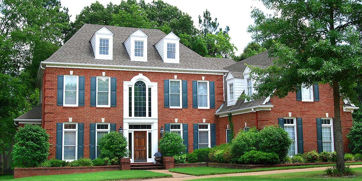 House plan exterior: Two-story brick home with three dormers, arched entryway, and dark green shutters.