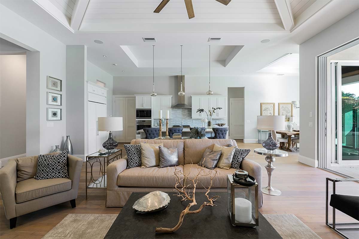 Interior rendering of a great room with beamed ceiling, open to a kitchen with island and dining area, featuring sliding glass doors.