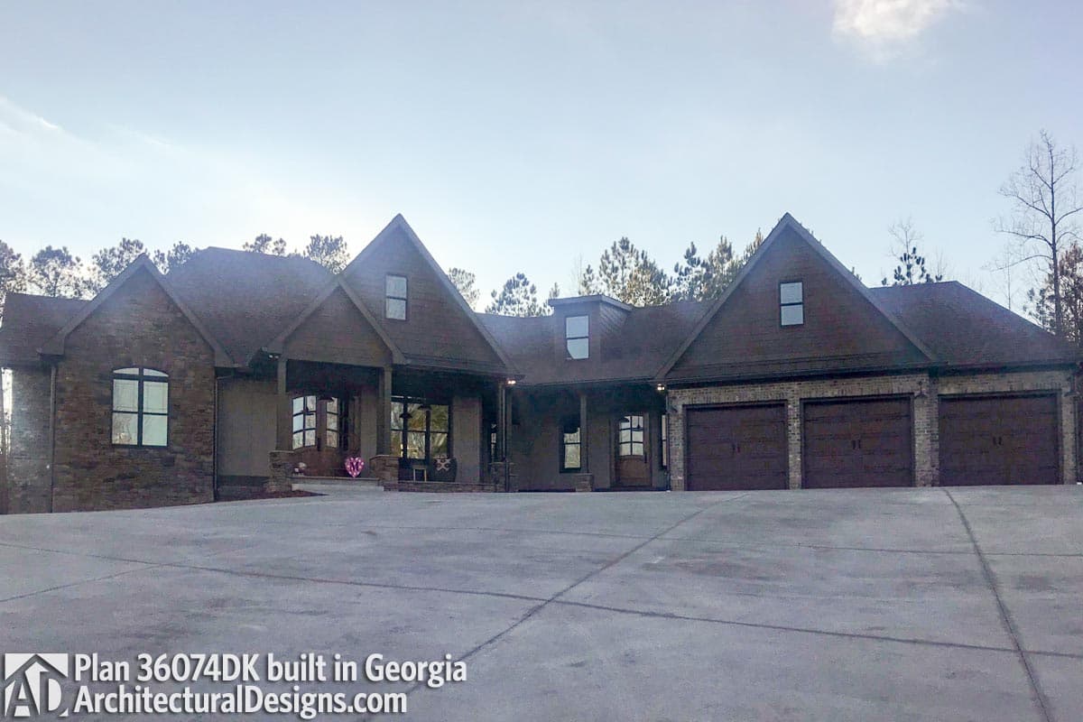 House plan exterior: One-story home with stone accents, prominent gables, covered entry porch, and a three-car garage.