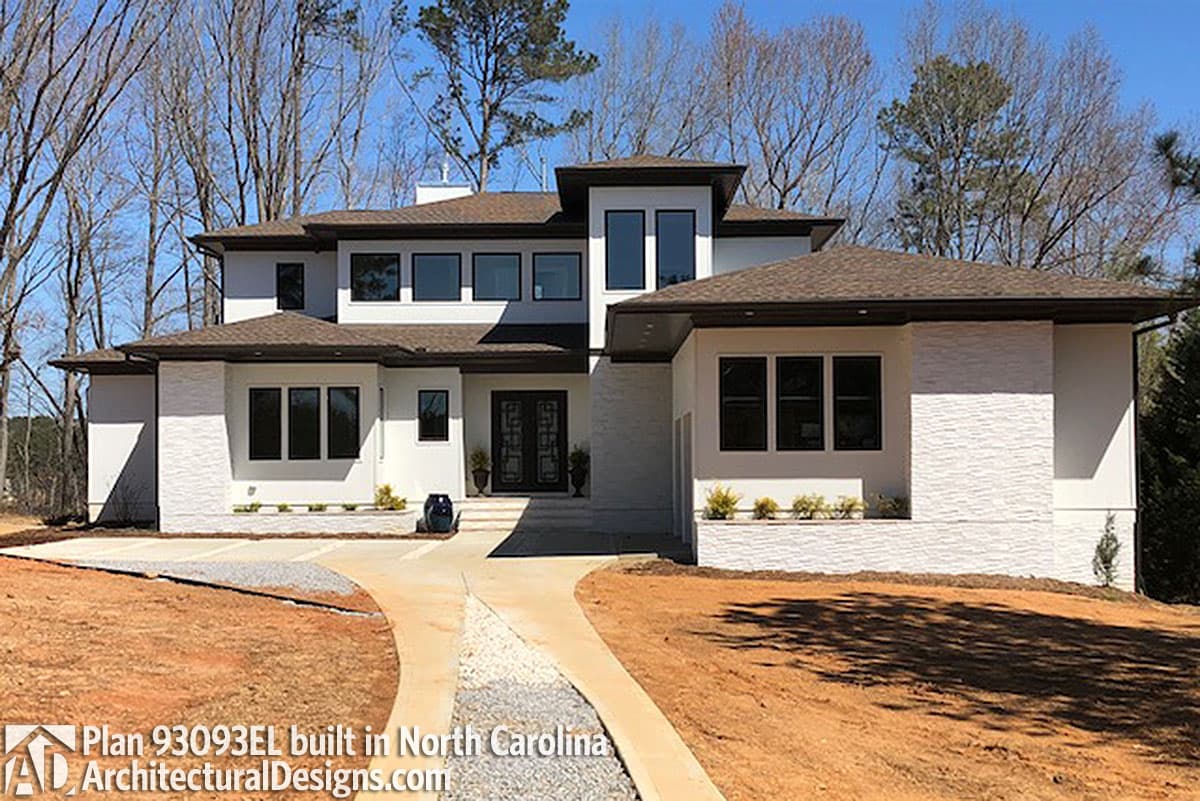 House plan exterior: Modern two-story residence with a white stucco and stone facade, flat roof sections, and multiple gabled rooflines.