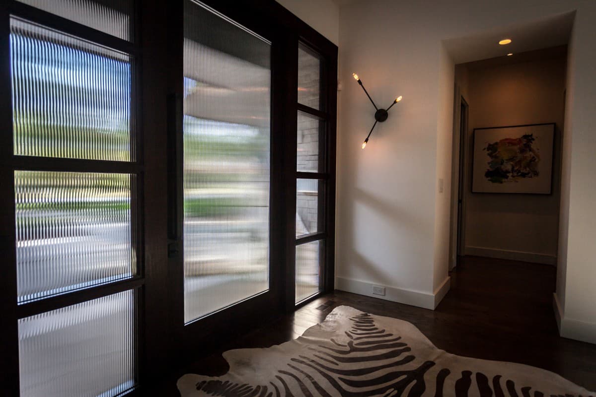 Entryway with dark wood doors featuring fluted glass, abstract art, and a modern wall sconce.
