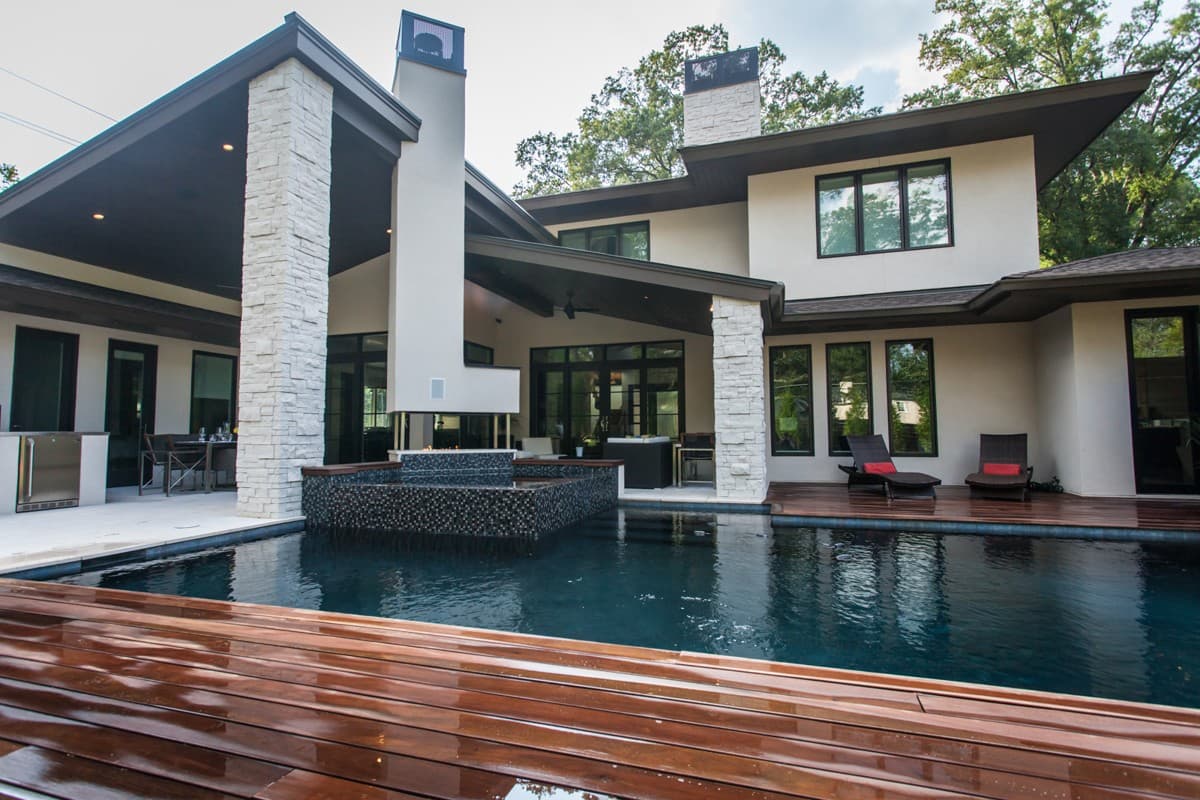 Modern house exterior with stone accents, covered patio, pool, and outdoor fireplace.
