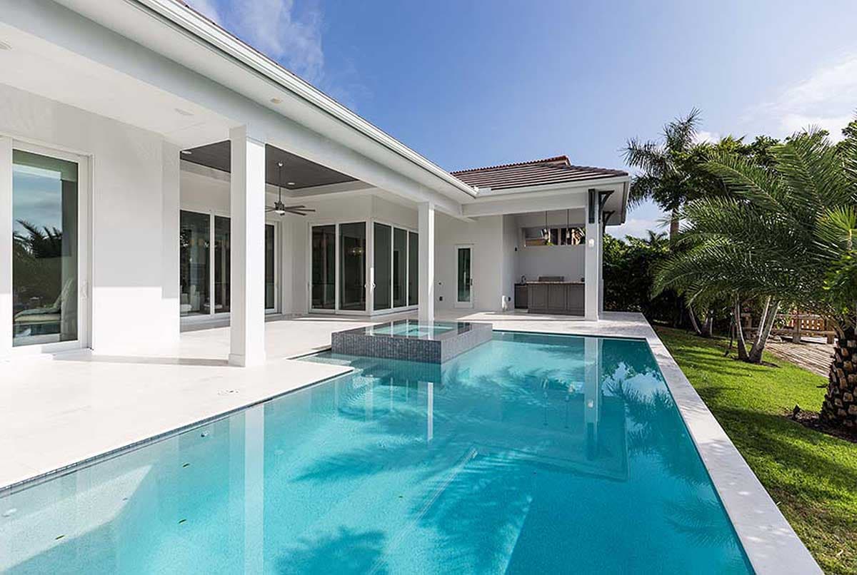 Modern house exterior with pool, covered patio, outdoor kitchen, and large glass doors.