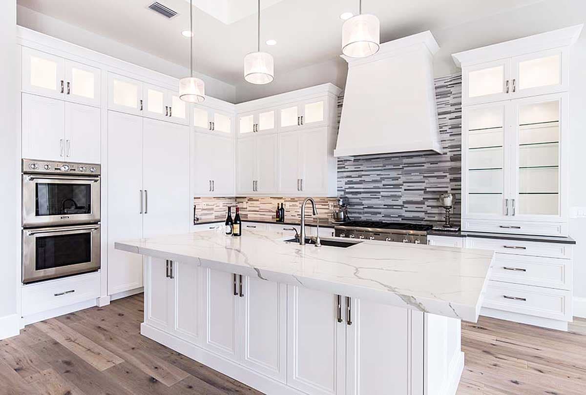 Modern kitchen with white cabinetry, marble island, stainless steel double oven and range with decorative backsplash.