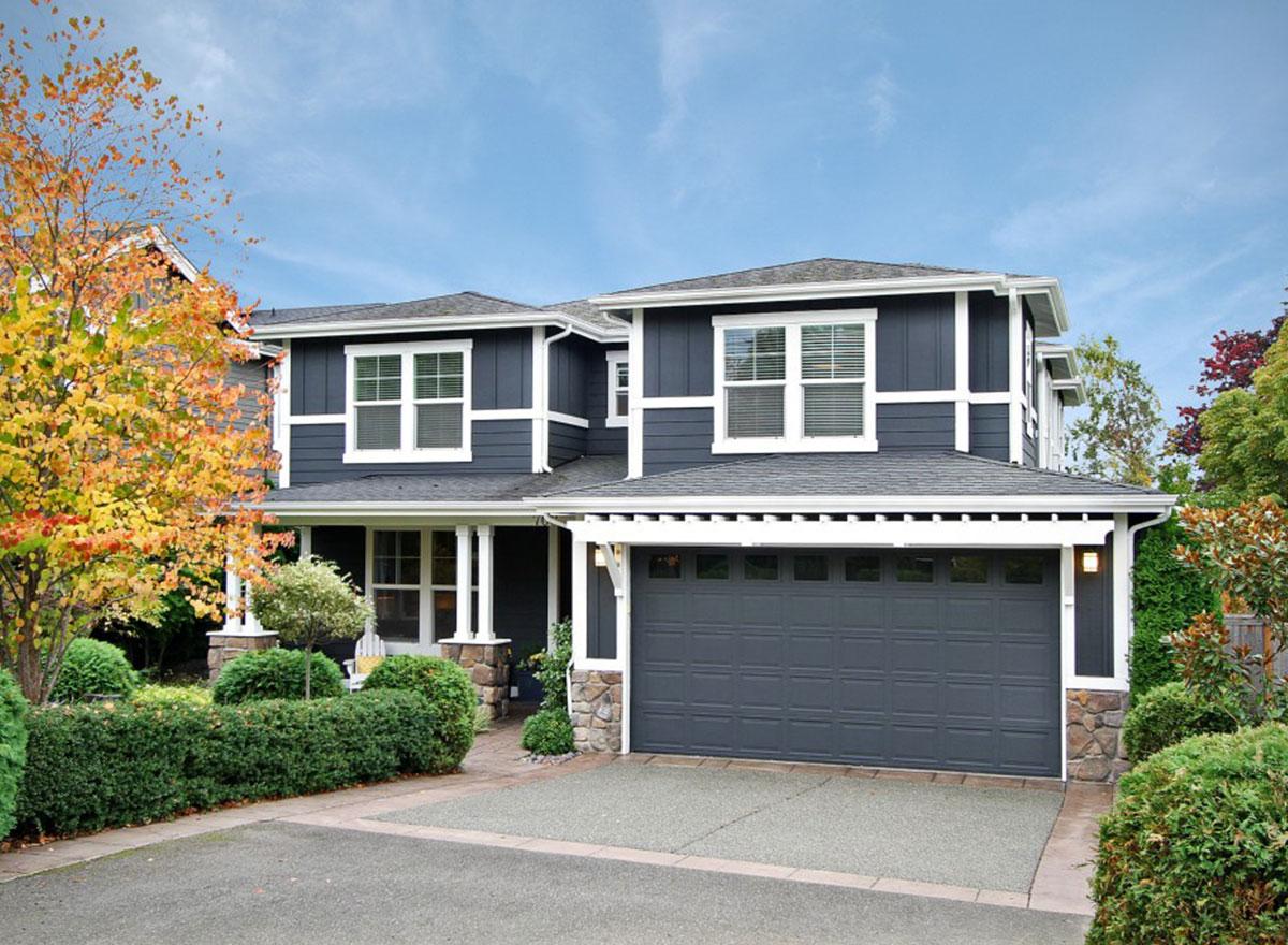 Two-story house plan exterior with dark siding, white trim, gabled roof, stone foundation, and attached two-car garage.