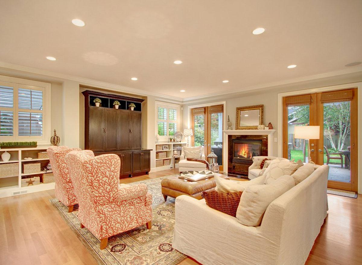 Living room with fireplace, large entertainment center, two patterned armchairs, a sectional sofa, and French doors leading outside.