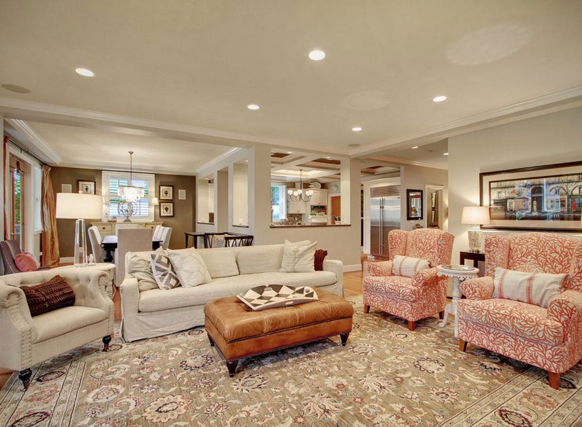 Open-concept living room with a large sofa, patterned armchairs, leather ottoman, and view into the dining area and kitchen.