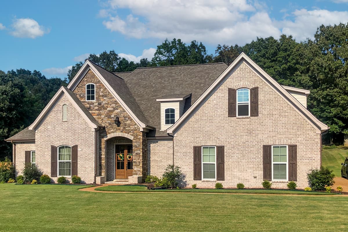House plan exterior. Two-story, brick facade, featuring gabled roof, stone archway over front door, and multiple dormers with shutters.