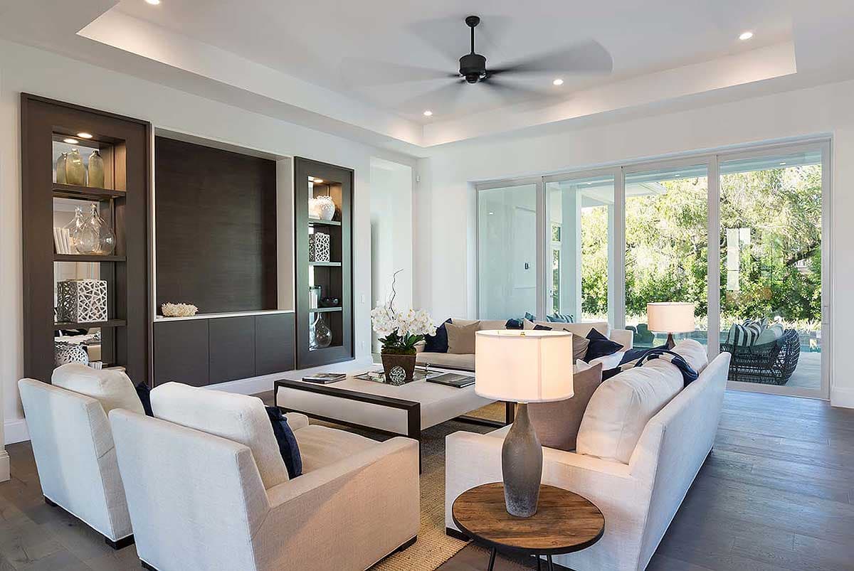 Contemporary living room with built-in shelving, tray ceiling, and sliding glass doors leading outdoors.