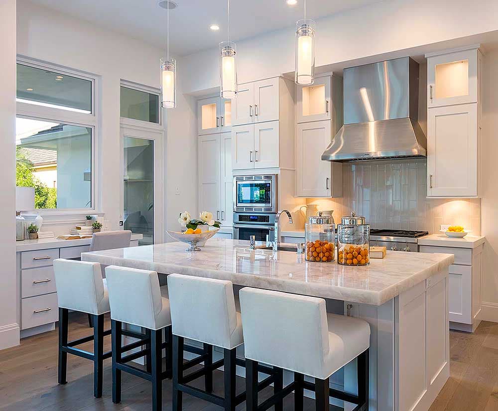 Kitchen with large island, white cabinets, stainless steel range hood, and ample counter space.