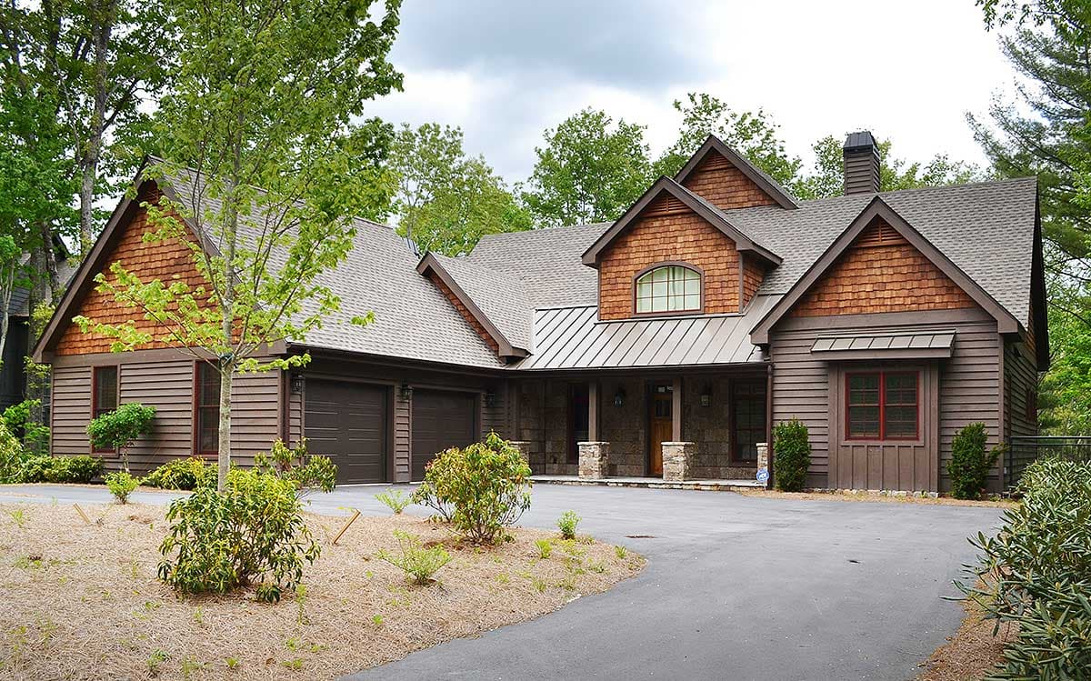 House plan exterior: Two-story mountain-style home with cedar shingles, metal roof accents, and a three-car garage.