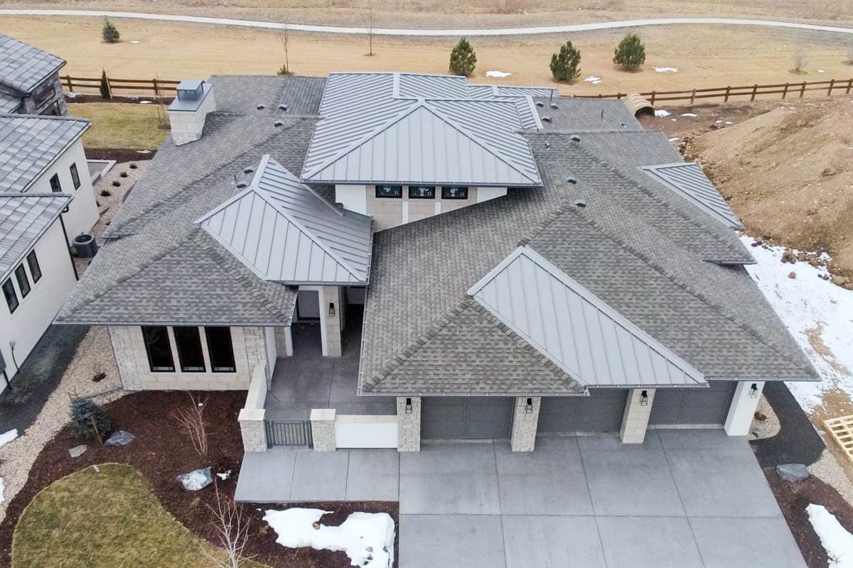 House plan exterior featuring a complex roofline with asphalt shingles and metal standing seam elements, a three-car garage, and stone accents.