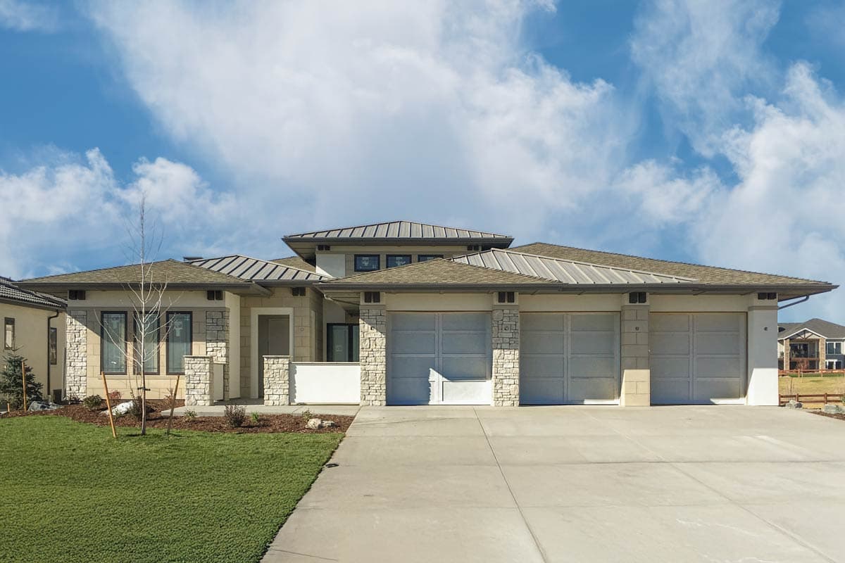 House plan exterior. Modern style, single story. Features include a three-car garage, stone accents, and a low-sloped roofline with metal accents.