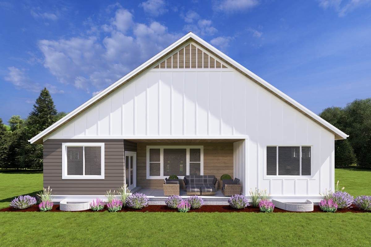 A modern white and brown house with a prominent gabled roof and a covered patio area with wicker furniture; the lawn is green.