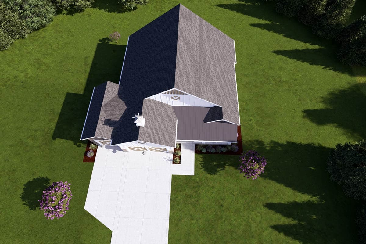 Aerial view of a house with a large gray roof and white accents. A concrete driveway leads to the house, surrounded by green lawn and trees.