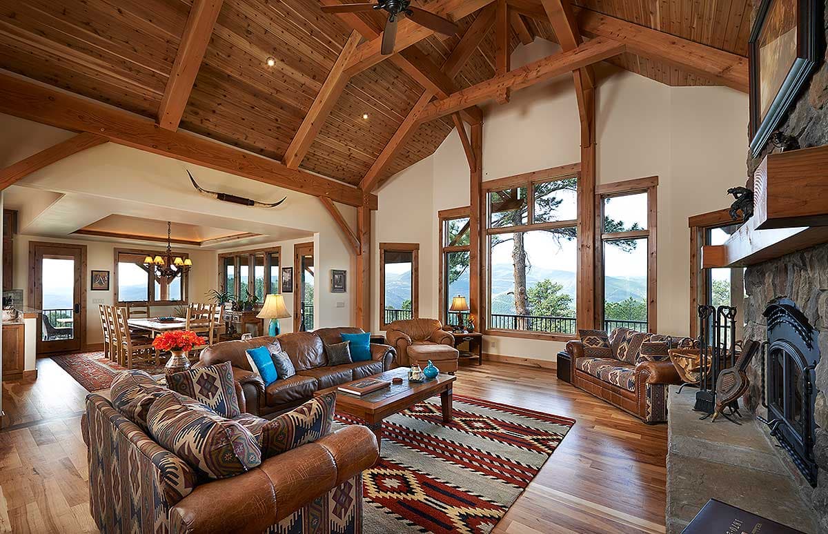 Great room with vaulted wooden beam ceiling, stone fireplace, and large windows with mountain views.