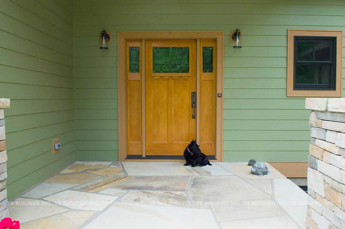 House plan exterior: wooden front door with sidelights, two lanterns, and stone pillar.