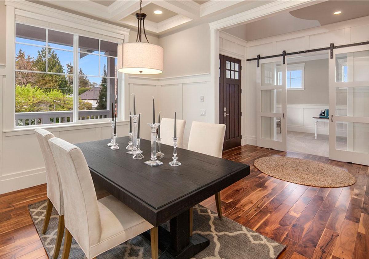 Dining room with dark wood table, beige chairs, coffered ceiling, and barn doors opening to another room.