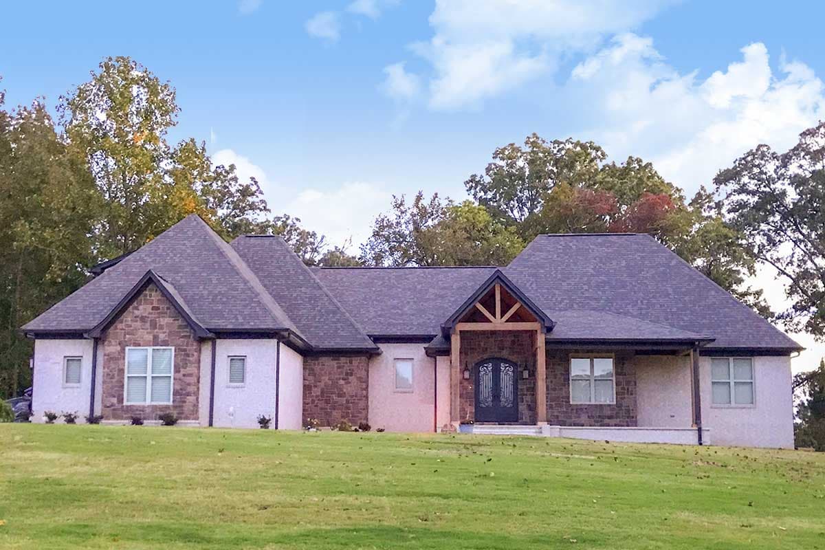House plan exterior. One-story house with stone and stucco facade. Features include gabled roof, timber frame entry porch, and varying rooflines.