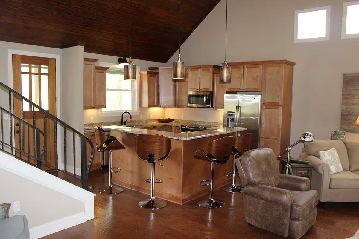 Interior view of a kitchen with a large island, stainless steel appliances, wood cabinetry, and a vaulted wood ceiling.