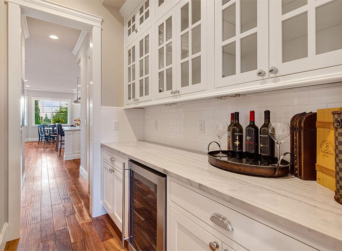 Butler's pantry with white subway tile backsplash, marble countertop, wine cooler, and glass-front cabinetry.