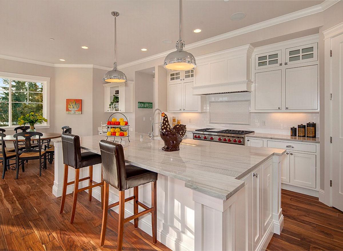 Kitchen with large island, white cabinetry, stainless steel range, pendant lights, and adjacent dining area with window.