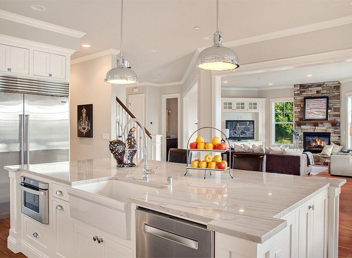Kitchen island with farmhouse sink, integrated microwave, and pendant lights, open to living room with stone fireplace and entertainment center.